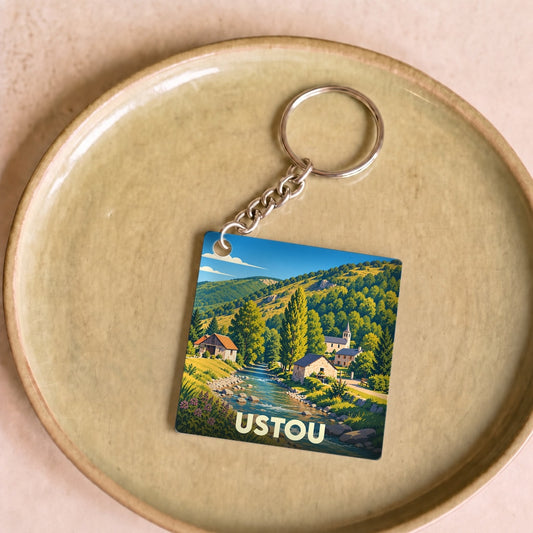 Porte-clés souvenir de la ville d'Ustou avec une illustration stylisée d'un paysage montagneux.