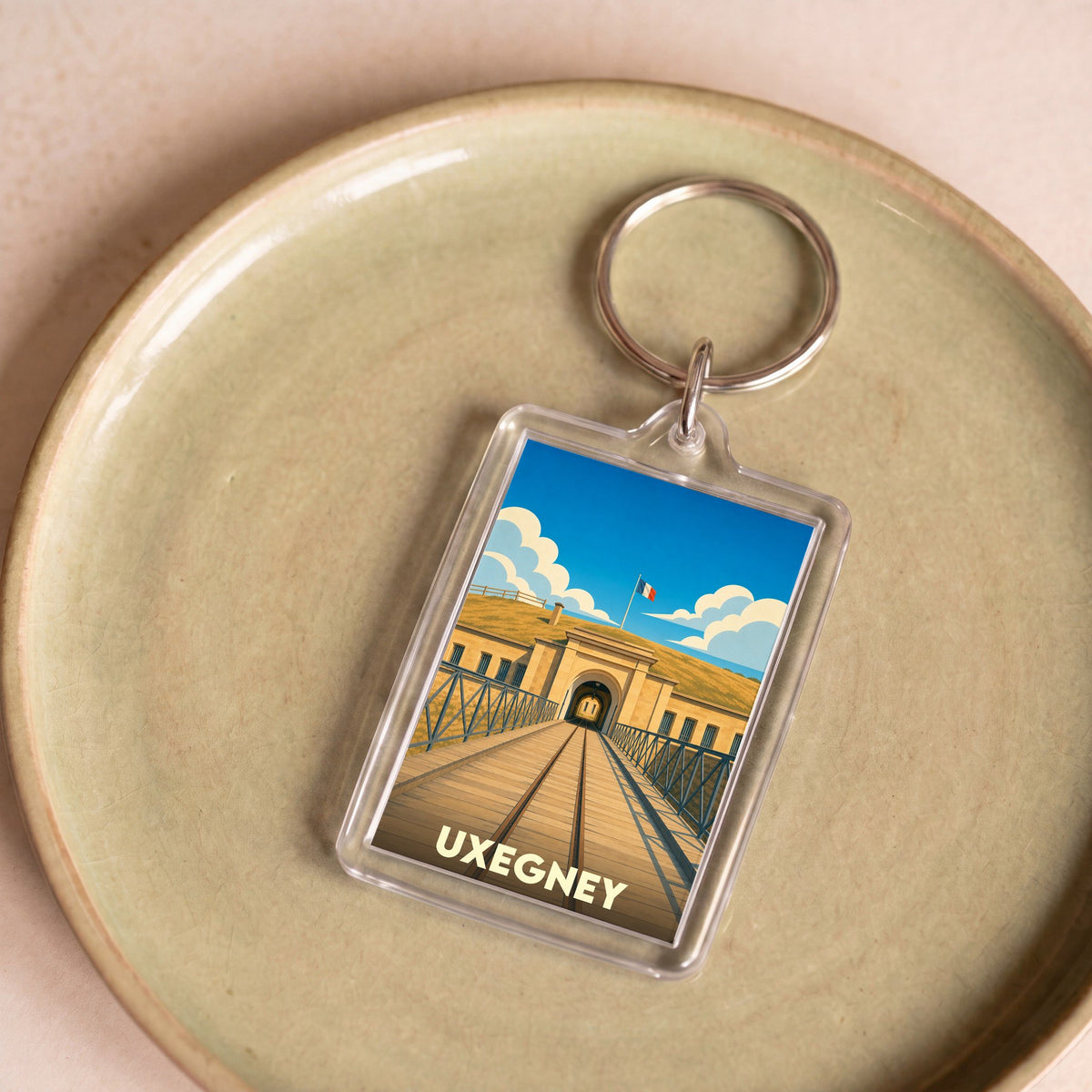 Porte-clés souvenir de la ville d'Uxegney avec une illustration stylisée de son fort historique.