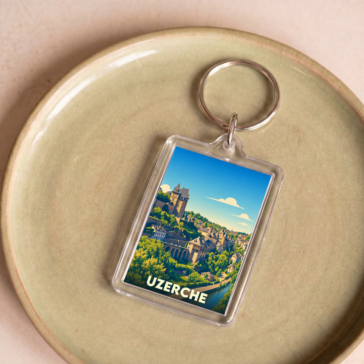 Porte-clés souvenir de la ville d'Uzerche avec une illustration stylisée de ses bâtiments historiques et de sa rivière.