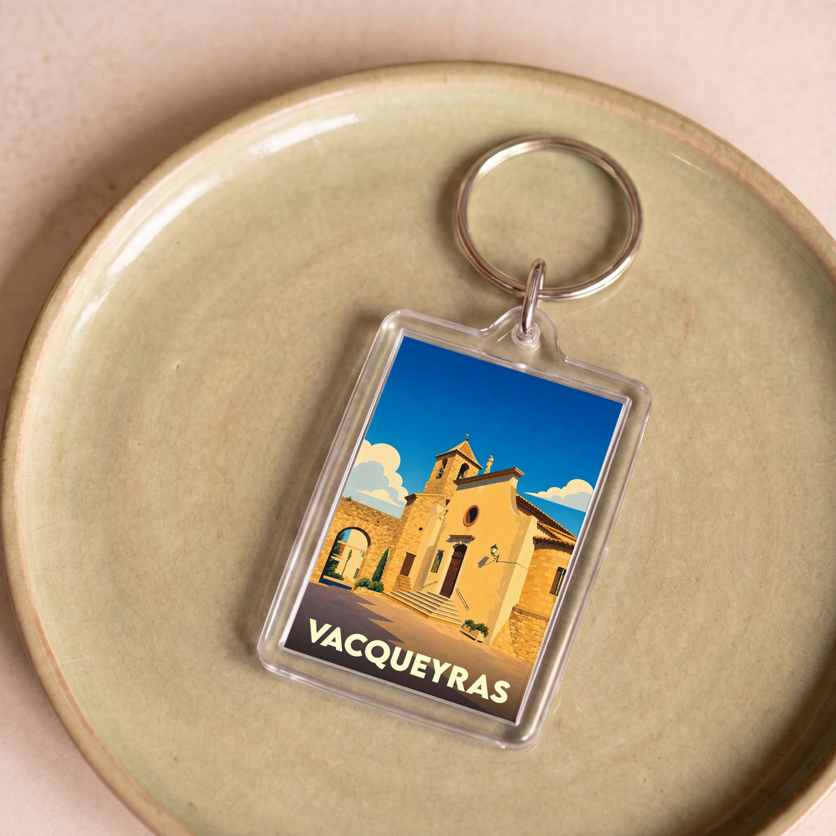Porte-clés souvenir de la ville de Vacqueyras avec une illustration stylisée de l'église locale sous un ciel bleu.