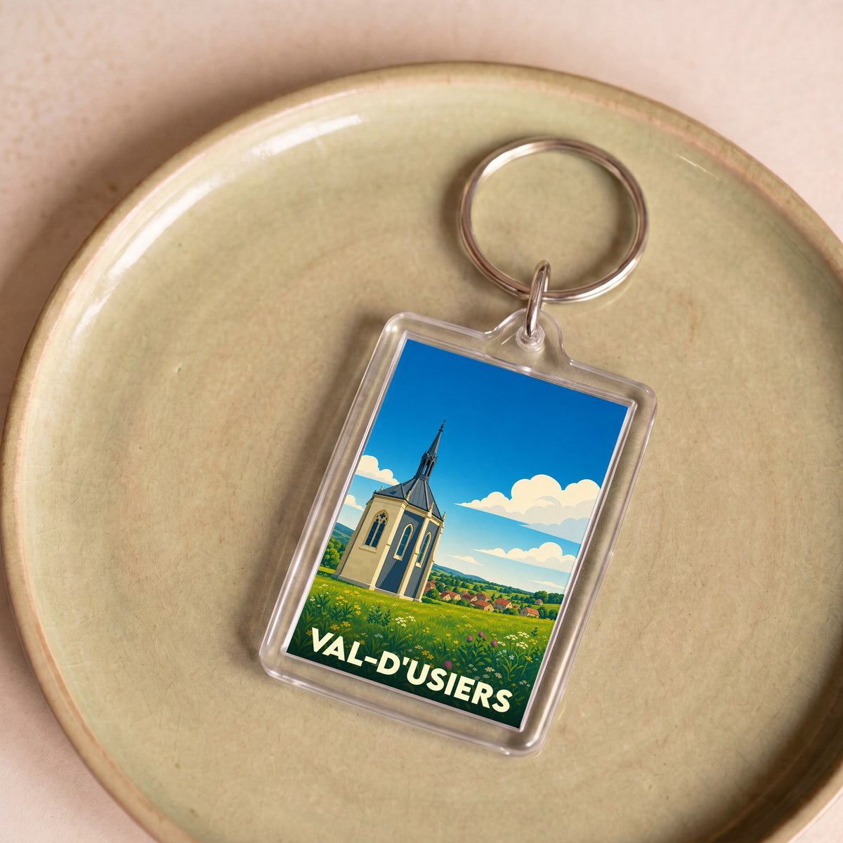 Porte-clés souvenir de Val-d'Usiers avec une illustration stylisée d'une chapelle dans un paysage verdoyant.