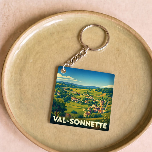 Porte-clés souvenir de la ville de Val-Sonnette avec une illustration stylisée de son paysage rural.