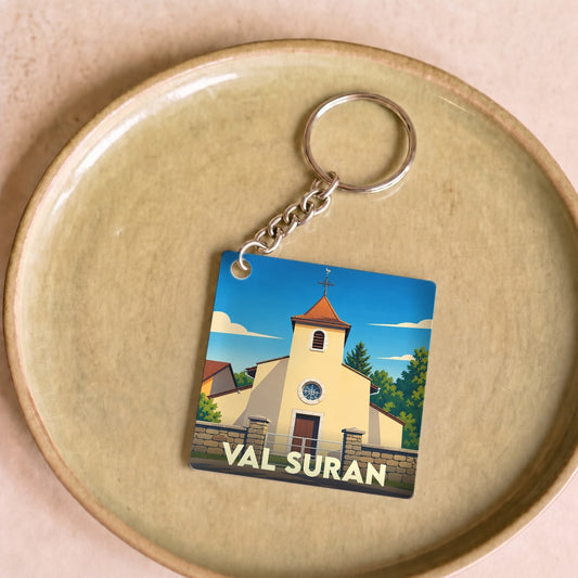 Porte-clés souvenir de la ville de Val Suran avec une illustration stylisée d'une église sous un ciel bleu.