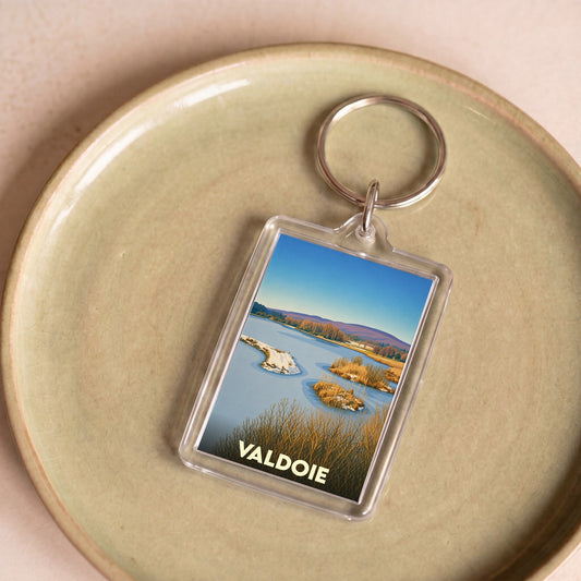 Porte-clés souvenir de la ville de Valdoie avec une illustration stylisée d'un paysage naturel.