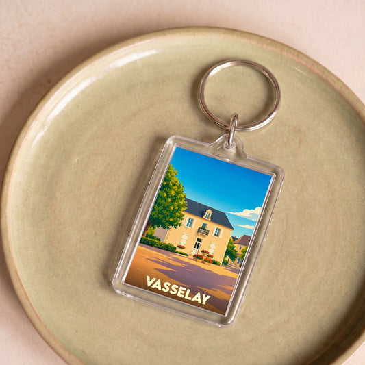 Porte-clés souvenir de la ville de Vasselay avec une illustration stylisée d'une maison de campagne sous un ciel bleu.