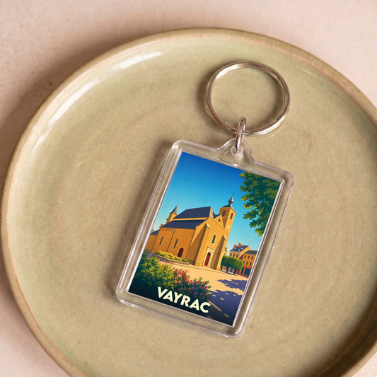 Porte-clés souvenir de la ville de Vayrac avec une illustration stylisée de son église sous un ciel bleu.