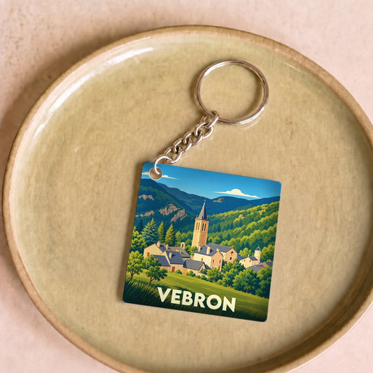 Porte-clés souvenir de la ville de Vebron avec une illustration stylisée de son clocher et de ses montagnes.