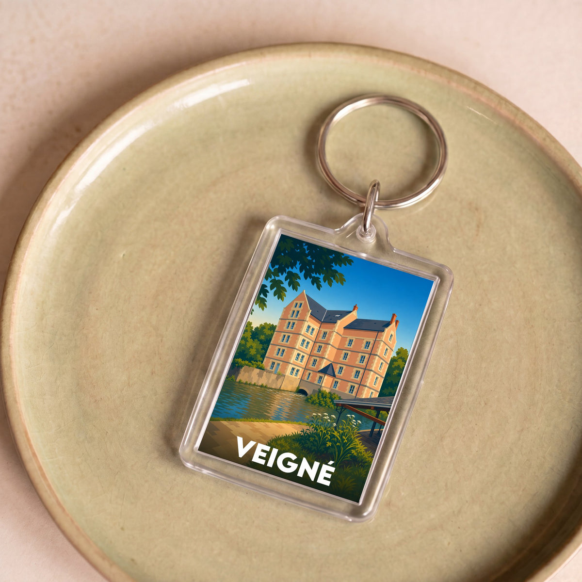 Porte-clés souvenir de la ville de Veigné avec une illustration stylisée d'un château au bord de l'eau.