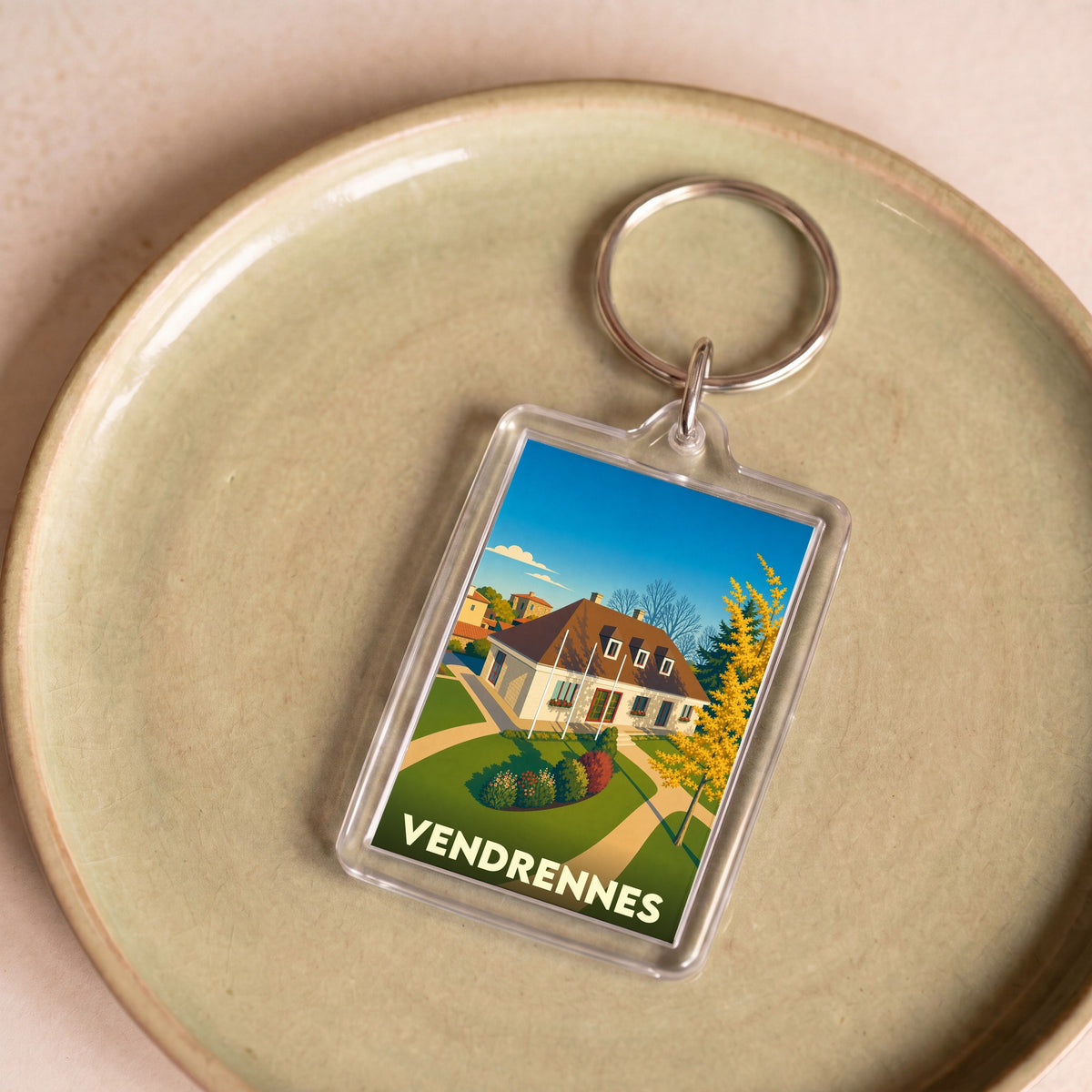 Porte-clés souvenir de la ville de Vendrennes avec une illustration stylisée d'une maison de campagne.