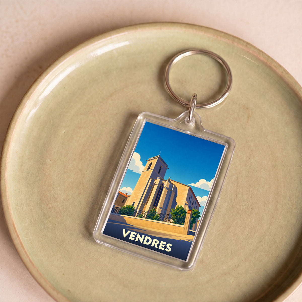 Porte-clés souvenir de la ville de Vendres avec une illustration stylisée de son église sous un ciel bleu.