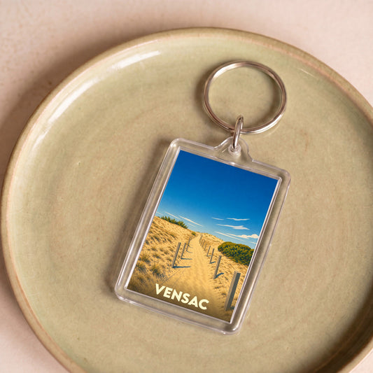 Porte-clés souvenir de la ville de Vensac avec une illustration stylisée d'un chemin à travers les dunes.