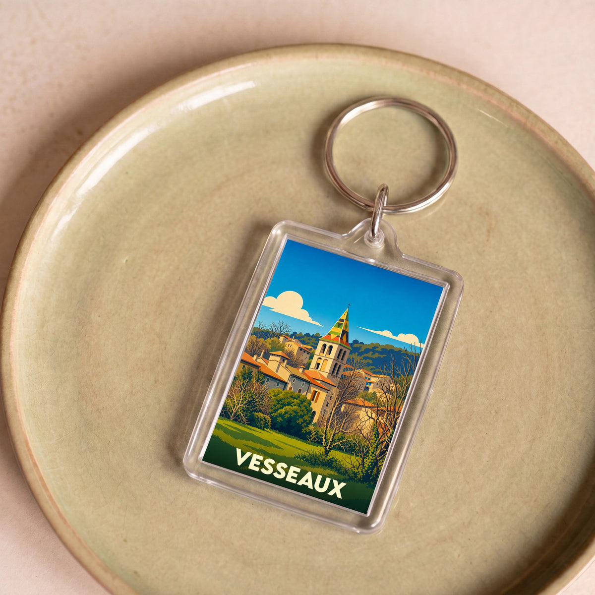 Porte-clés souvenir de la ville de Vesseaux avec une illustration stylisée de son église et de ses paysages.