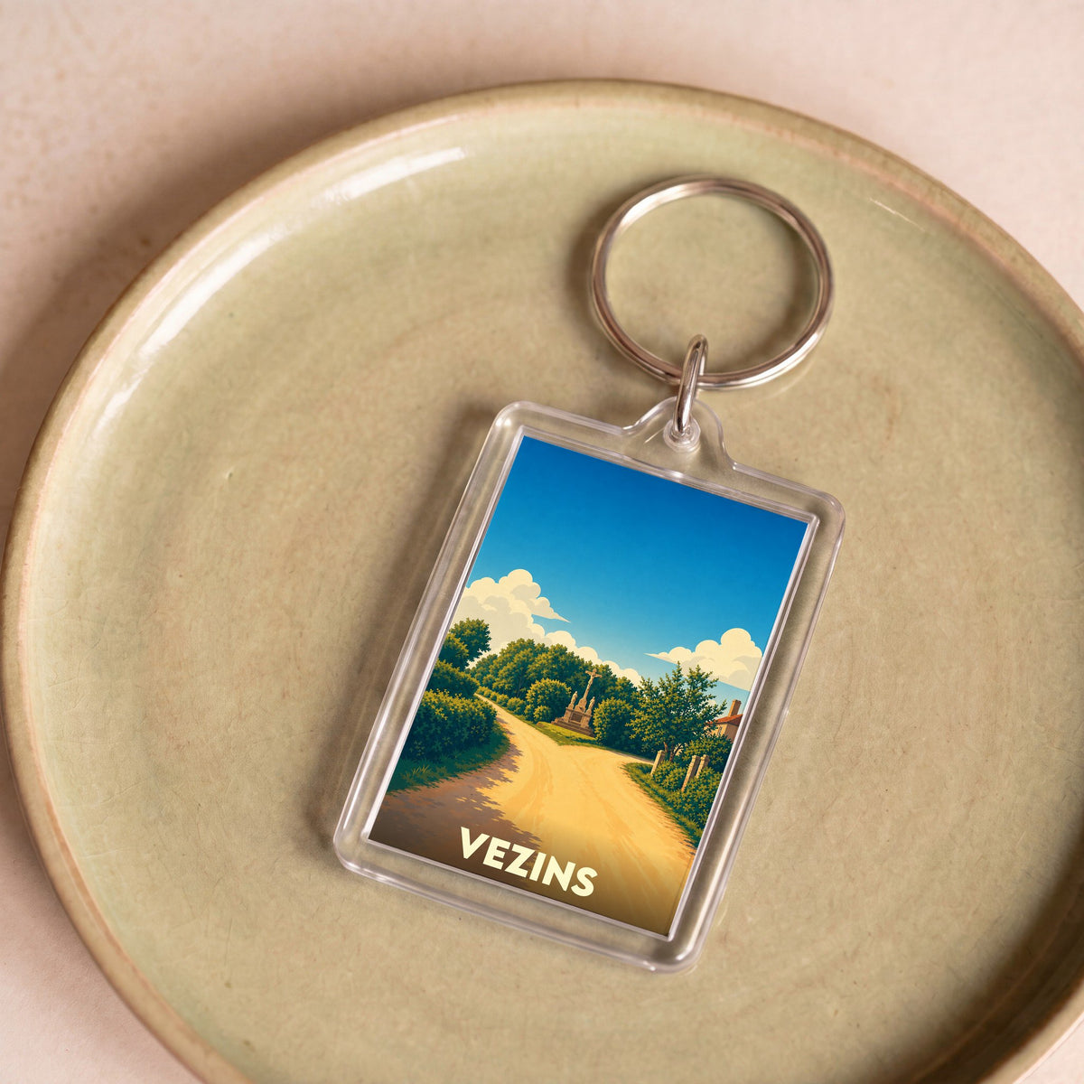 Porte-clés souvenir de la ville de Vezins avec une illustration stylisée d'un chemin de campagne.