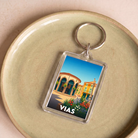 Porte-clés souvenir de la ville de Vias avec une illustration stylisée et colorée.