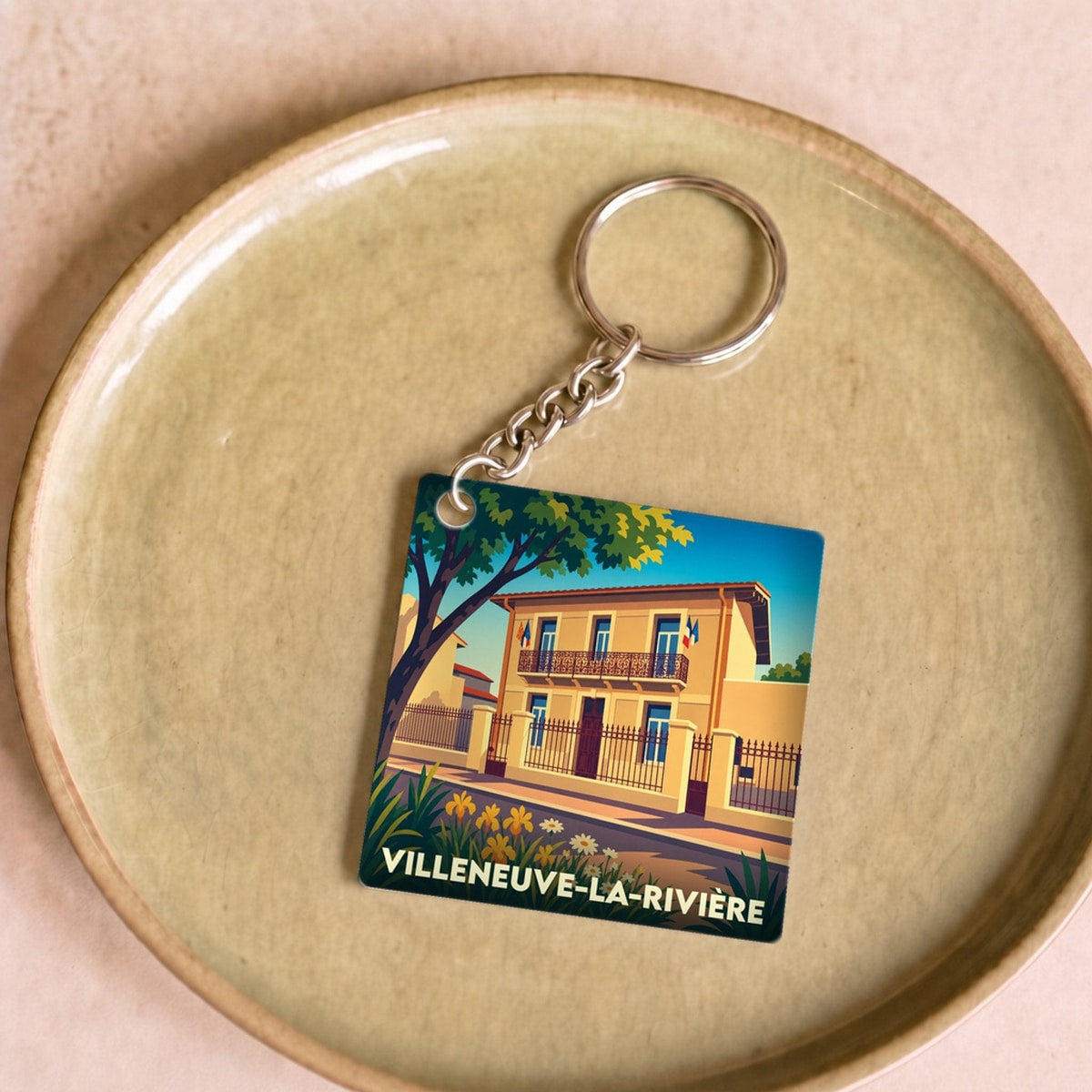 Porte-clés souvenir de la ville de Villeneuve-la-Rivière avec une illustration stylisée d'une maison typique.