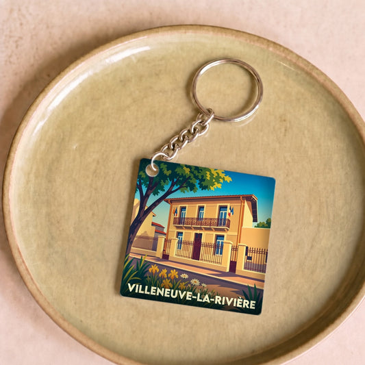 Porte-clés souvenir de la ville de Villeneuve-la-Rivière avec une illustration stylisée d'une maison typique.