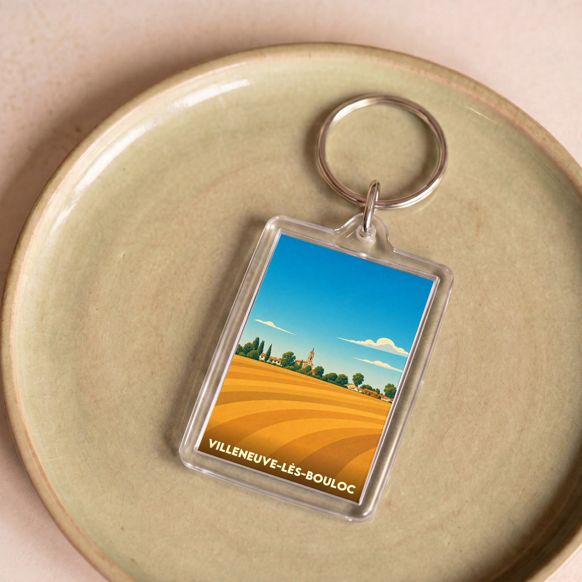 Porte-clés souvenir de la ville de Villeneuve-lès-Bouloc avec une illustration stylisée de champs dorés et d'un village.