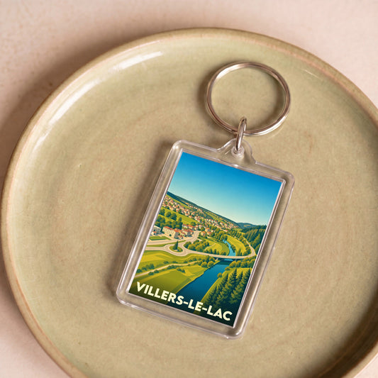 Porte-clés souvenir de la ville de Villers-le-Lac avec une illustration stylisée d'un paysage de vallée.