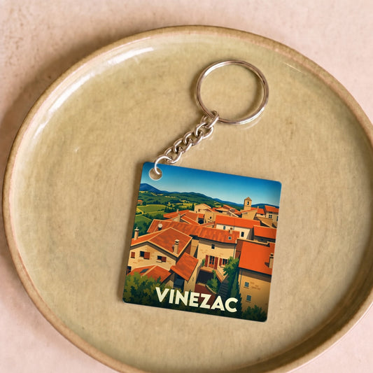 Porte-clés souvenir de la ville de Vinezac avec une illustration stylisée de ses toits provençaux.