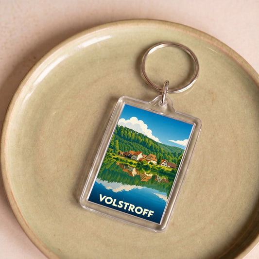 Porte-clés souvenir de la ville de Volstroff avec une illustration stylisée d'un paysage lacustre.