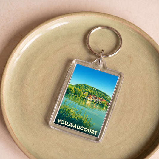 Porte-clés souvenir de la ville de Voujeaucourt avec une illustration stylisée d'un paysage de bord de rivière.