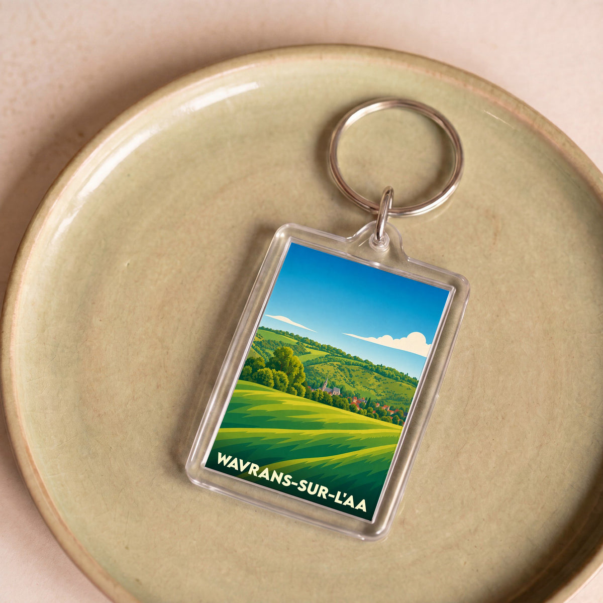 Porte-clés souvenir de la ville de Wavrans-sur-l'Aa avec une illustration stylisée de paysages vallonnés.