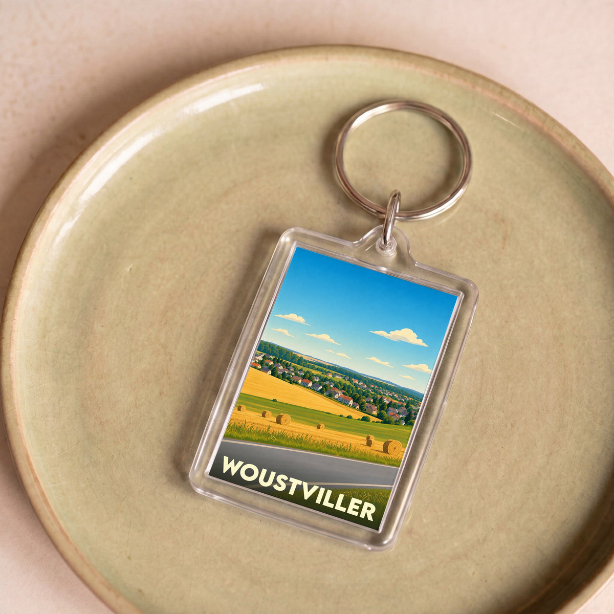Porte-clés souvenir de la ville de Woustviller avec une illustration stylisée de paysages ruraux.