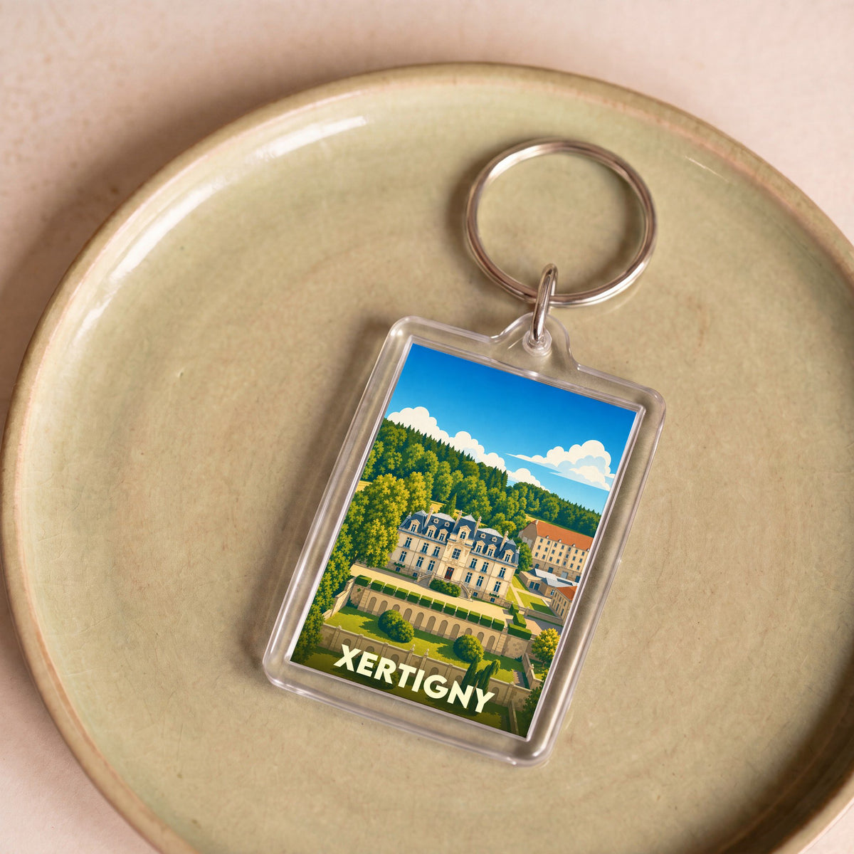 Porte-clés souvenir de la ville de Xertigny avec une illustration stylisée d'un château entouré de jardins.