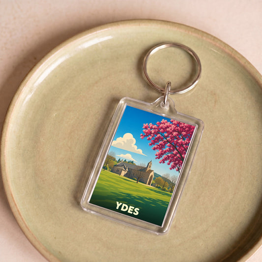 Porte-clés souvenir de la ville d'Ydes avec une illustration stylisée d'une église et d'un arbre en fleurs.