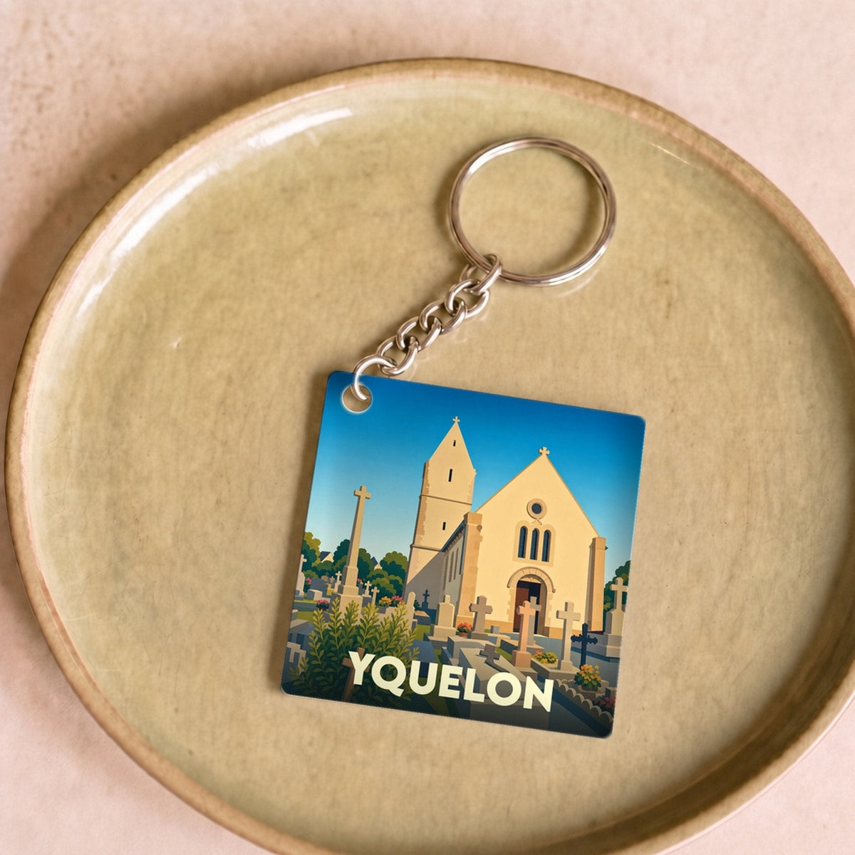 Porte-clés souvenir de la ville d'Yquelon avec une illustration stylisée d'une église et de son cimetière.