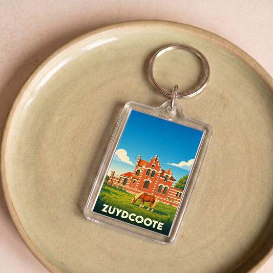 Porte-clés souvenir de la ville de Zuydcoote avec une illustration stylisée d'un bâtiment flamand et d'un cheval.