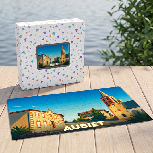 Puzzle souvenir de la ville d'Aubiet avec une illustration stylisée d'une place ensoleillée et son église.