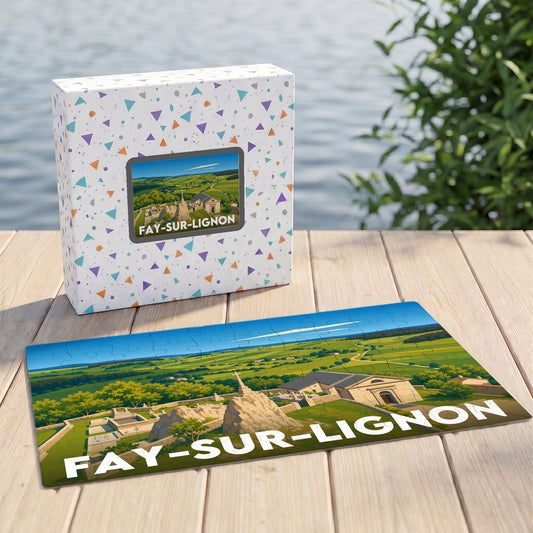 Puzzle souvenir de Fay-sur-Lignon arborant une illustration paysagère stylisée, présenté à côté de sa boîte sur un ponton en bois.