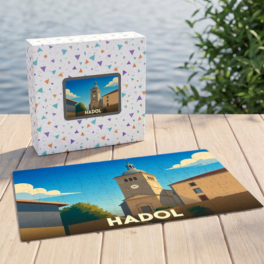 Puzzle souvenir de la ville de Hadol avec une illustration stylisée d'un clocher et de bâtiments ensoleillés.