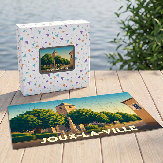 Puzzle souvenir de la ville de Joux-la-Ville avec son coffret, illustrant une place arborée et son église dans un style graphique épuré.