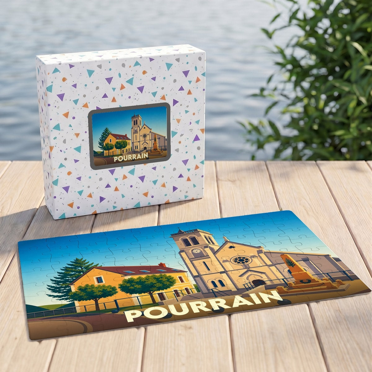 Puzzle souvenir de la ville de Pourrain accompagné de sa boîte, illustrant l'église et les bâtiments locaux dans un style graphique épuré.