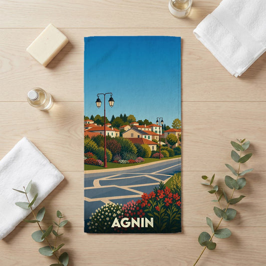 Serviette de bain souvenir de la ville d'Agnin avec une illustration stylisée d'un paysage urbain fleuri.