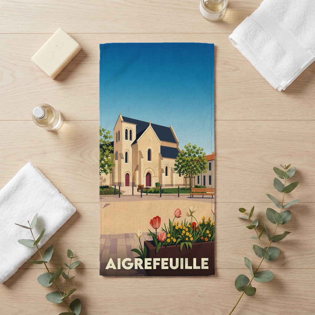 Serviette de bain souvenir de la ville d’Aigrefeuille avec une illustration stylisée de son église.