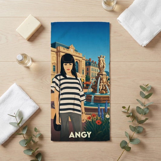 Serviette de bain souvenir de la ville d'Angy avec une illustration stylisée d'une femme devant une fontaine.