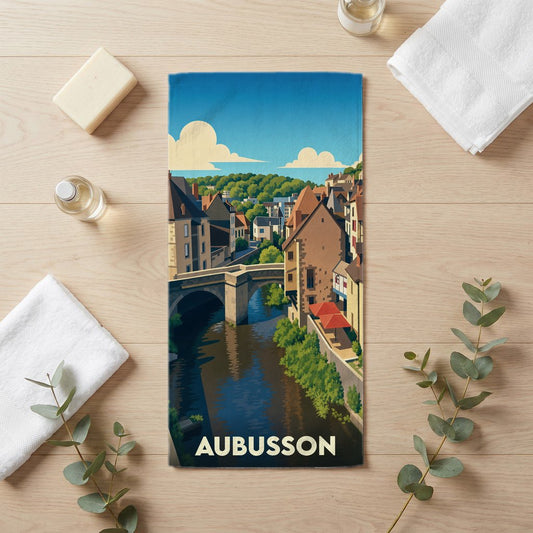 Serviette de bain souvenir de la ville d'Aubusson illustrée d'un paysage urbain stylisé avec pont et rivière.