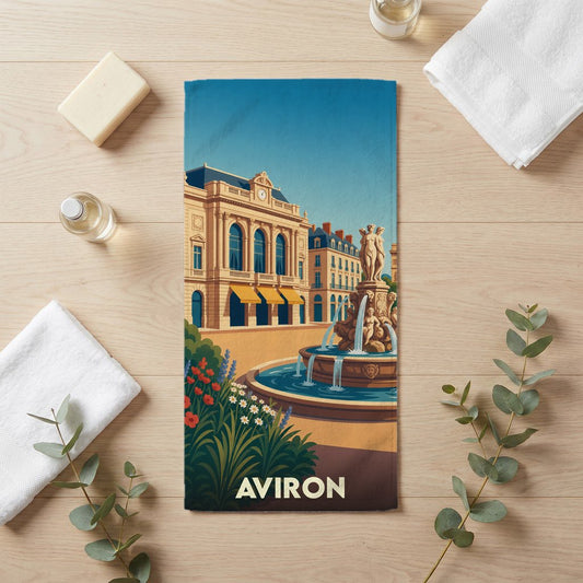 Serviette de bain souvenir de la ville d'Aviron avec une illustration stylisée d'une place ensoleillée et sa fontaine.