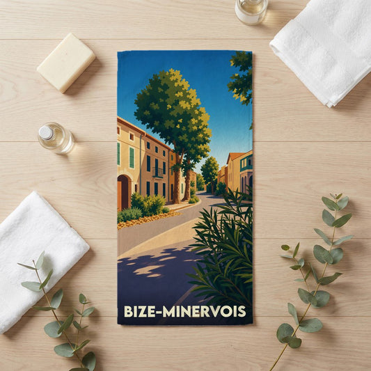 Serviette de bain souvenir de la ville de Bize-Minervois illustrée d'une rue ensoleillée aux façades colorées.
