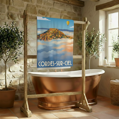 Serviette de bain souvenir de la ville de Cordes-sur-Ciel avec une illustration stylisée du village émergeant des nuages.