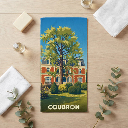 Serviette de bain souvenir de la ville de Coubron illustrée par une demeure bourgeoise et un grand arbre stylisé.