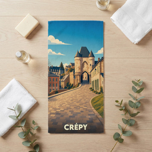 Serviette de bain souvenir de la ville de Crépy illustrée par une vue stylisée d'une porte médiévale et d'une rue pavée.