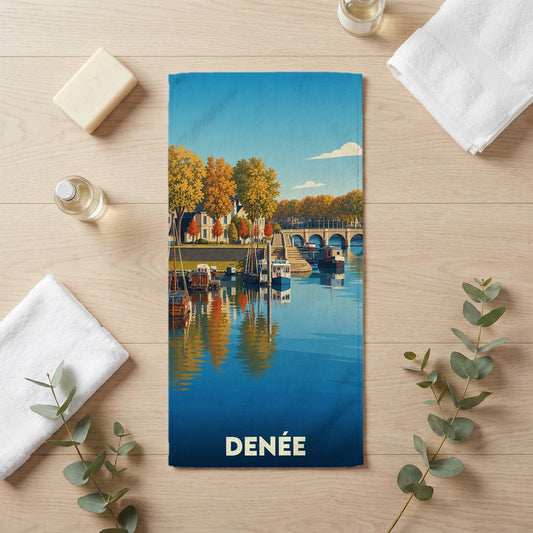 Serviette de bain souvenir de la ville de Denée avec une illustration stylisée d'un paysage de bord d'eau.