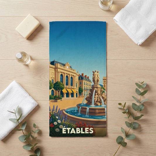 Serviette de bain souvenir de la ville d'Étables avec une illustration stylisée d'une fontaine et d'un bâtiment historique.