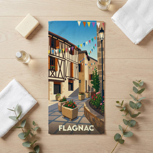 Serviette de bain souvenir de la ville de Flagnac avec une illustration stylisée d'une rue pittoresque.