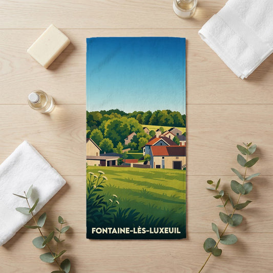 Serviette de bain souvenir de Fontaine-lès-Luxeuil avec une illustration de paysage rural stylisée.