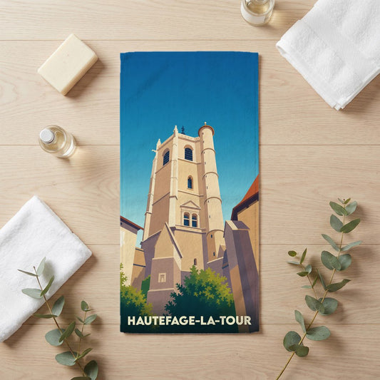 Serviette de bain souvenir de Hautefage-la-Tour avec une illustration stylisée de sa tour médiévale.